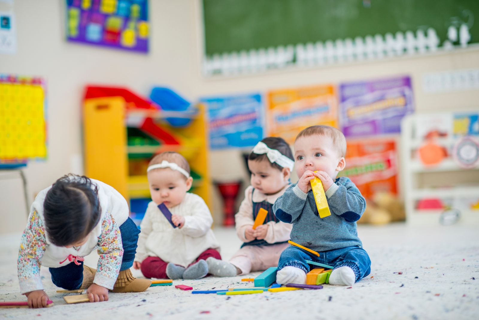 Four infants playing with colorful blocks on a classroom floor